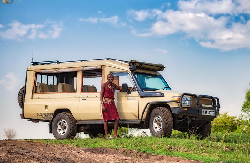 Maasai guide standing next to safari Land Cruiser Kenya
